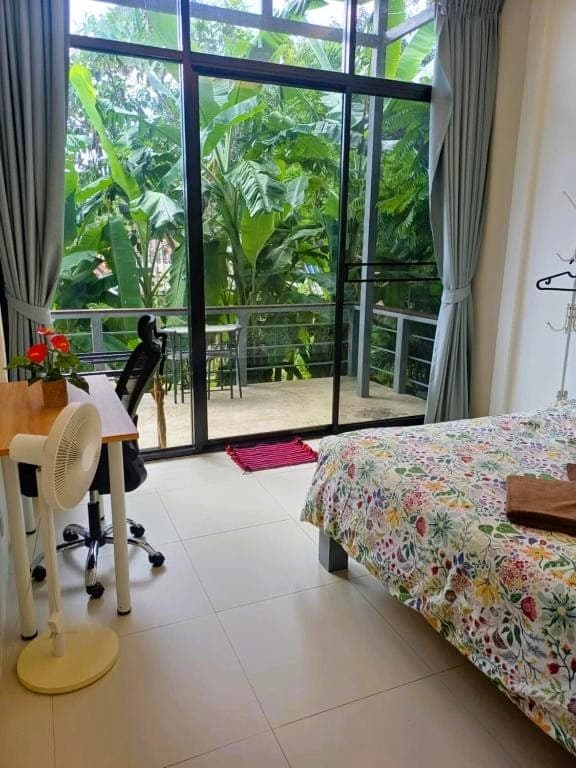 Modern Bungalow 1 — large white floor tile, a desk with an office chair, a floor fan and full-height balcony doors onto the banana trees